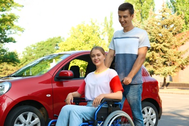 Young man with disabled woman in wheelchair near car outdoors