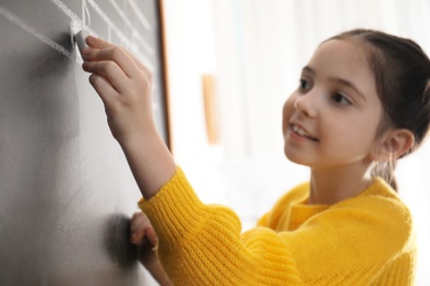 Little girl writing music notes on blackboard in classroom, closeup