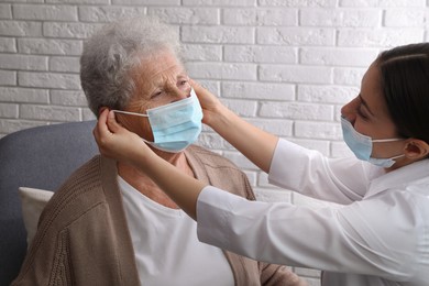 Doctor putting protective mask on senior woman at nursing home