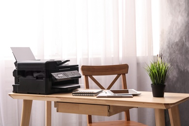 Photo of Modern printer, tablet and office supplies on wooden table indoors