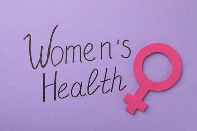 Female gender sign near text Women's Health on violet background, top view