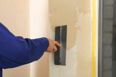 Professional worker plastering window area with putty knife indoors, closeup. Interior repair