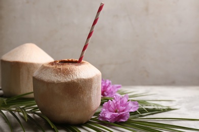 Young peeled coconuts with straw, palm leaf and beautiful flowers on grey table. Space for text