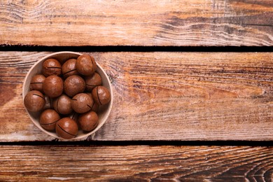 Photo of Delicious organic Macadamia nuts in bowl on wooden table, top view. Space for text