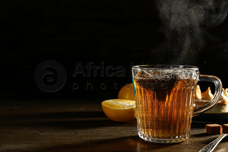 Photo of Tea bag in glass cup of hot water on dark wooden table. Space for text
