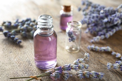 Bottle of natural essential oil and lavender flowers on wooden background