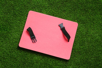 Pink foam seat mat for tourist on green grass, top view