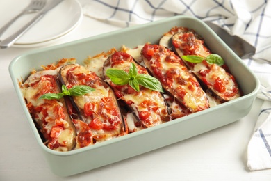 Baked eggplant with tomatoes, cheese and basil in dishware on white wooden table