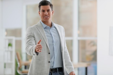 Businessman reaching out for handshake in office, focus on hand