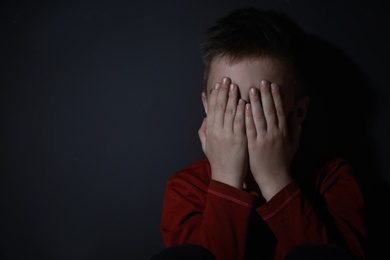 Scared little boy closing his eyes near black wall, space for text. Domestic violence concept