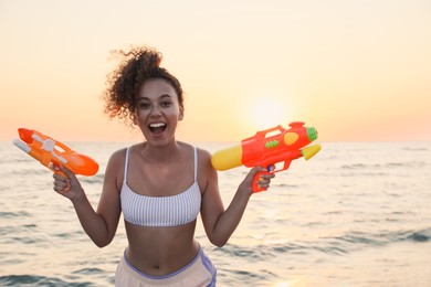African American woman with water guns having fun on beach at sunset