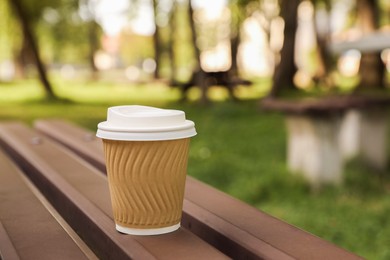 Paper cup on wooden bench in park, space for text. Coffee to go