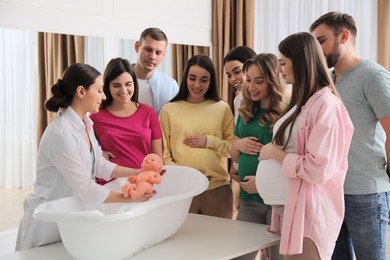 Pregnant women with men learning how to bathe baby at courses for expectant parents indoors