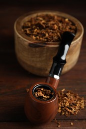 Smoking pipe and dry tobacco on wooden table, closeup