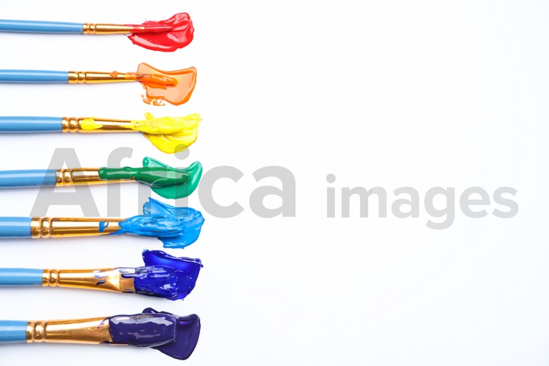 Set of brushes with different paints on white background, flat lay. Rainbow colors
