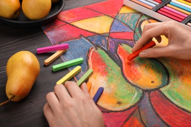 Woman drawing pears on paper with soft pastels at wooden table, closeup