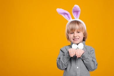 Photo of Happy boy wearing bunny ears headband on orange background, space for text. Easter celebration