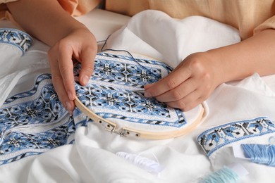 Woman embroidering shirt with blue thread at table, closeup. Ukrainian national clothes