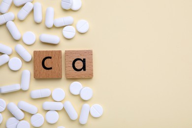 Wooden cubes with symbol Ca (Calcium) and pills on beige background, top view. Space for text