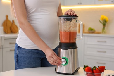 Young pregnant woman preparing smoothie at table in kitchen, closeup. Healthy eating