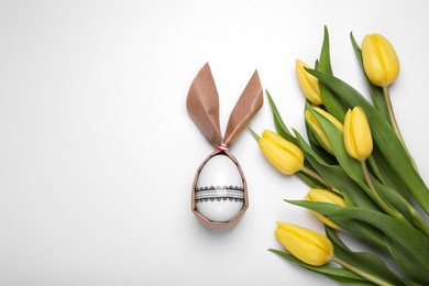 Photo of Easter bunny made of craft paper and egg near beautiful tulips on white background, flat lay. Space for text