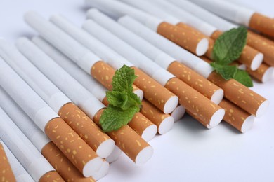 Menthol cigarettes and fresh mint leaves on white background, closeup
