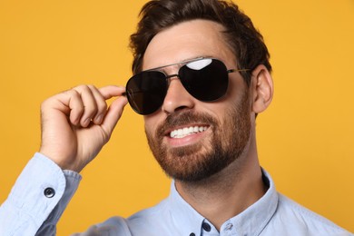 Portrait of smiling bearded man with stylish sunglasses on orange background, closeup