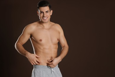 Fit man with marks on body against dark brown background, space for text. Weight loss surgery