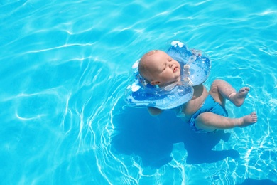 Cute little baby with inflatable neck ring in swimming pool on sunny day, outdoors