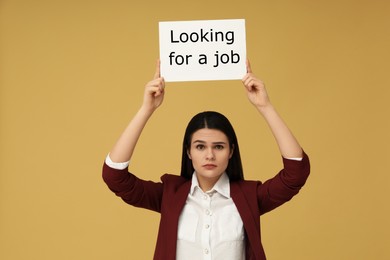 Photo of Unemployment problem. Unhappy woman holding sign with phrase Looking For A Job on pale orange background