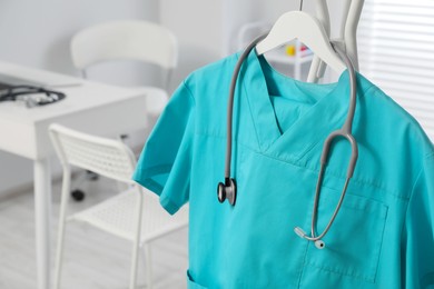 Photo of Turquoise medical uniform and stethoscope on rack in clinic, closeup. Space for text