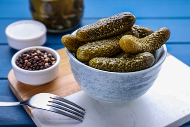 Bowl of pickled cucumbers and ingredients on blue wooden table, closeup