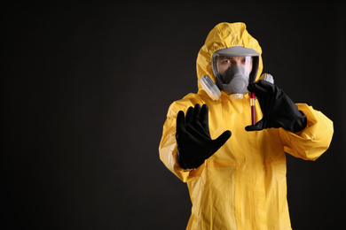 Man in chemical protective suit holding test tube of blood sample on black background, space for text. Virus research