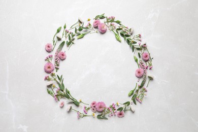 Wreath made of beautiful flowers and green leaves on light grey marble background, flat lay. Space for text