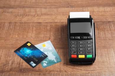 Modern payment terminal and credit cards on wooden background. Space for text