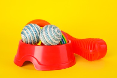 Various bright pet toys and bowl on yellow background