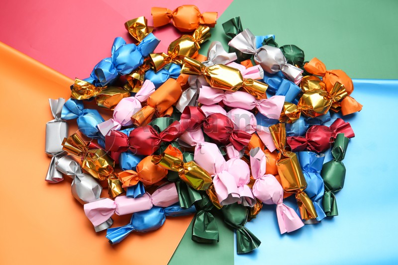 Many candies in different wrappers on color background, above view