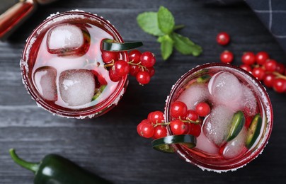 Photo of Glasses of spicy red currant cocktail with jalapeno on black wooden table, flat lay