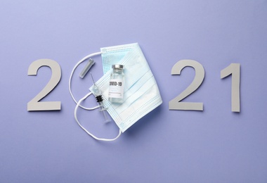 Paper numbers, medical mask, vial and syringe forming 2021 on violet background, flat lay. Coronavirus vaccination