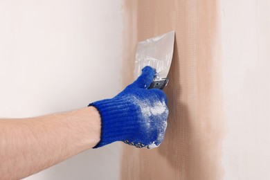 Worker plastering wall with putty knife indoors, closeup