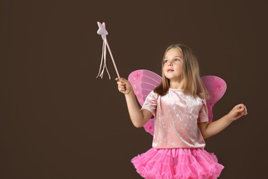Cute little girl in fairy costume with wings and magic wand on brown background. Space for text