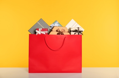 Paper shopping bag full of gift boxes on yellow background