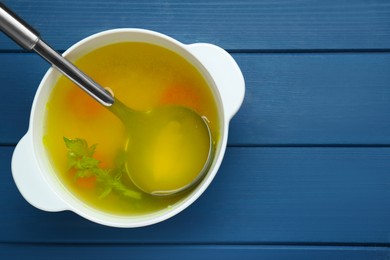 Photo of Delicious chicken bouillon with carrot and celery on blue wooden table, top view. Space for text