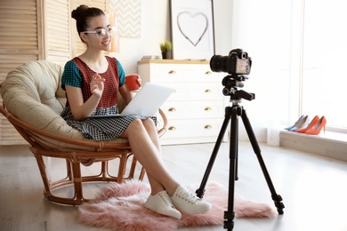 Young blogger with laptop in lounge chair recording video at home