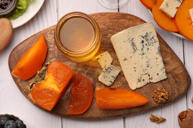 Photo of Delicious persimmon with blue cheese on white wooden table, flat lay