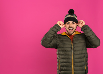 Happy young man in warm clothes on pink background, space for text. Winter vacation