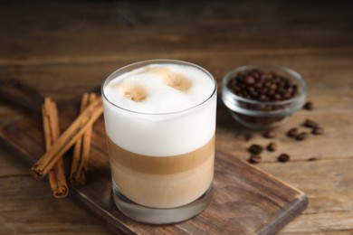 Delicious latte macchiato, cinnamon sticks and coffee beans on wooden table
