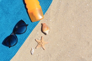 Photo of Stylish sunglasses, bottle of sunblock and blue towel on sand, flat lay with space for text. Beach accessories