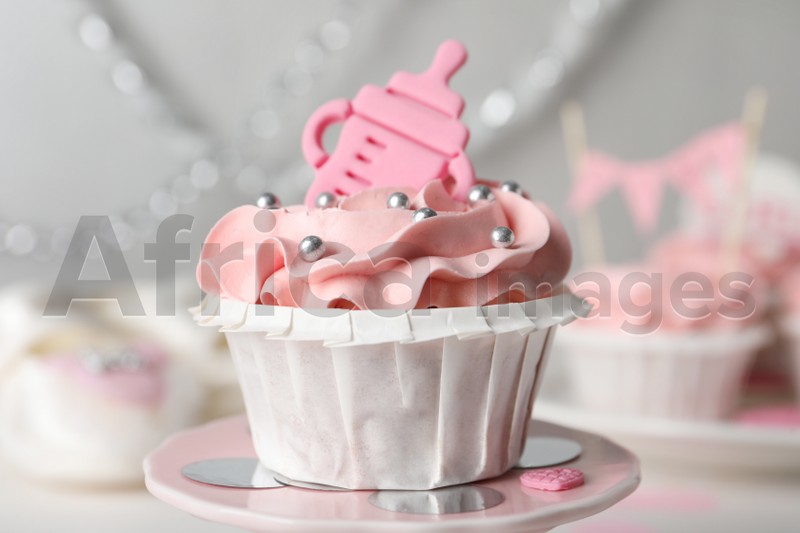 Photo of Delicious cupcake with pink cream and topper for baby shower on stand, closeup