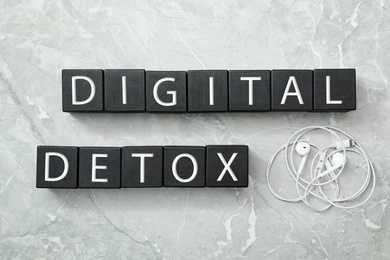 Black cubes with words DIGITAL DETOX and earphones on light grey marble background, flat lay